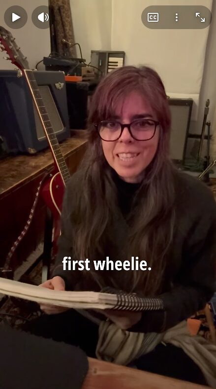 vlog 14 image of clara smiling holding a notebook with the text "first wheelie"
